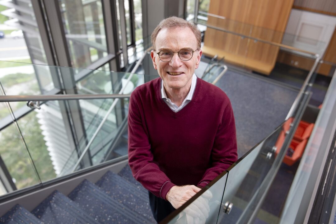 Randy Schekman, PhD, stands on a stairwell, wearing glasses, exuding a contemplative demeanor.