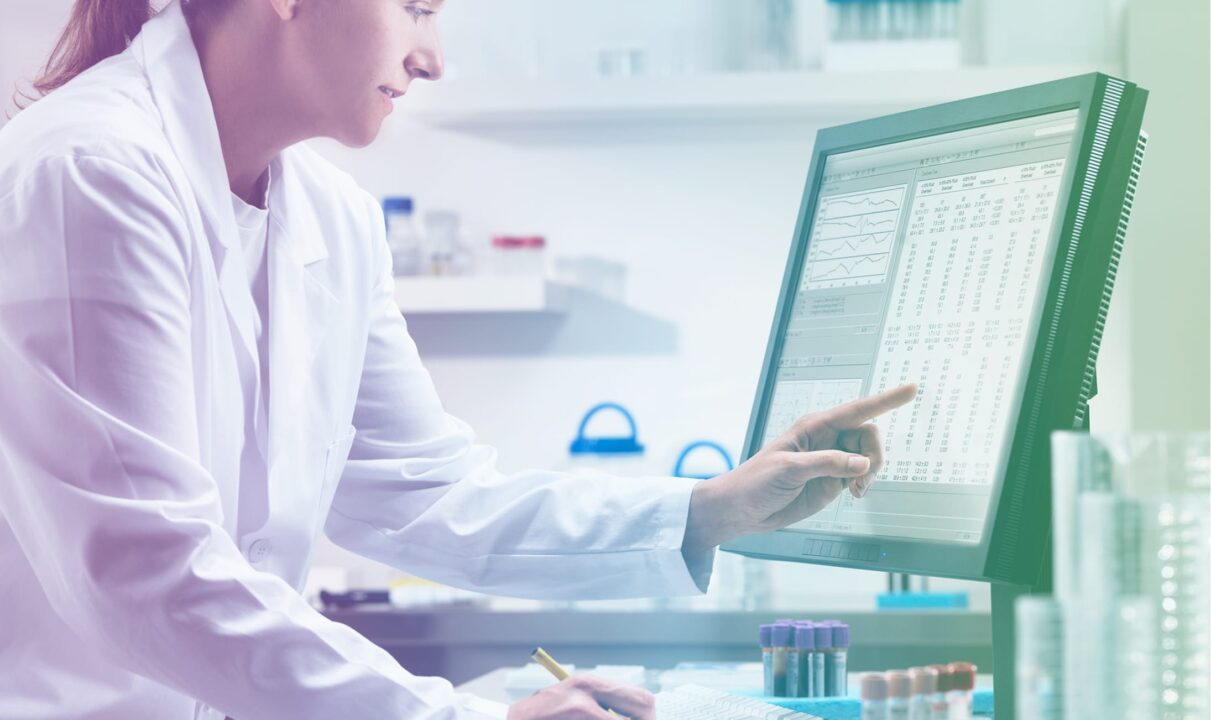 A female scientist in a lab coat analyzes information displayed on a computer screen