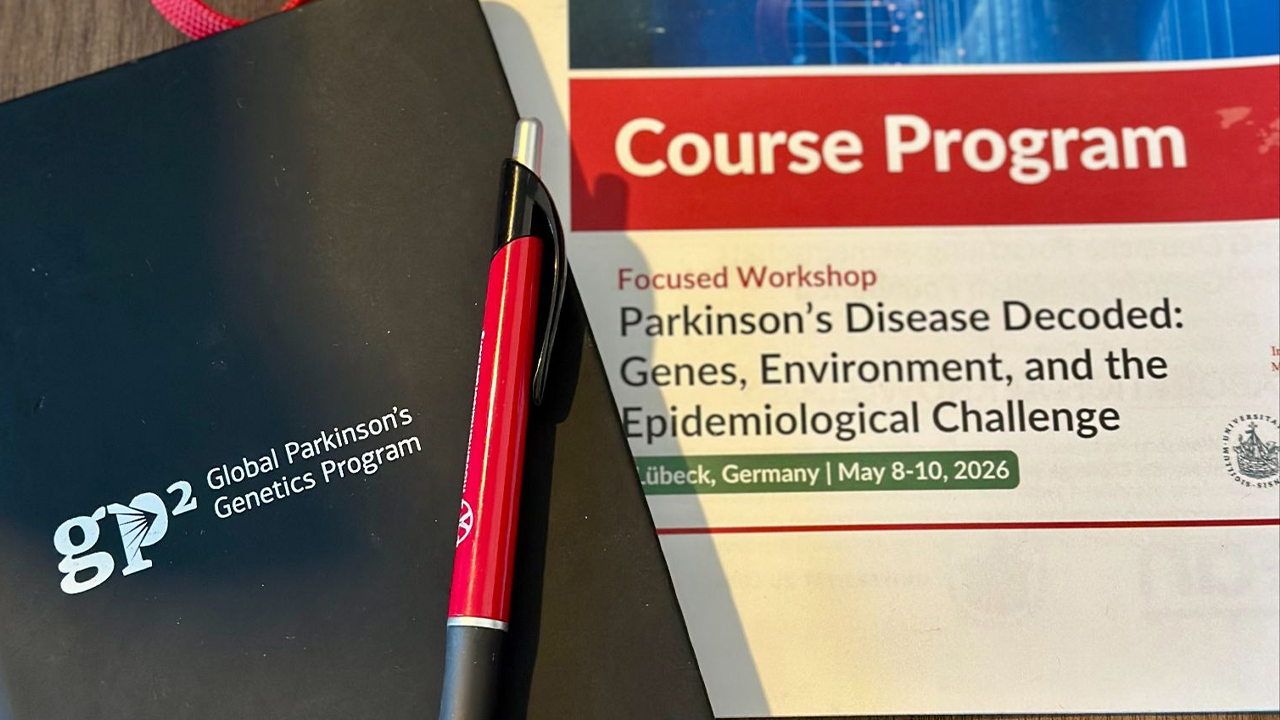 GP2-branded notebook and red pen beside the course program for “Parkinson’s Disease Decoded: Genes, Environment, and the Epidemiological Challenge,” held in Lübeck, Germany, May 8–10, 2026.